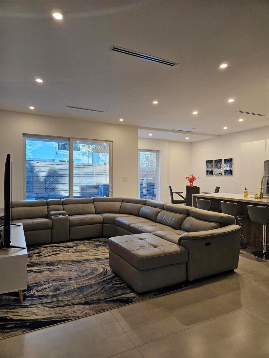 A modern living room features a large grey sectional sofa, a patterned rug, and kitchen — 2275 SE 7th Street, Pompano Beach FL 33062, POMPANO BEACH, FL
