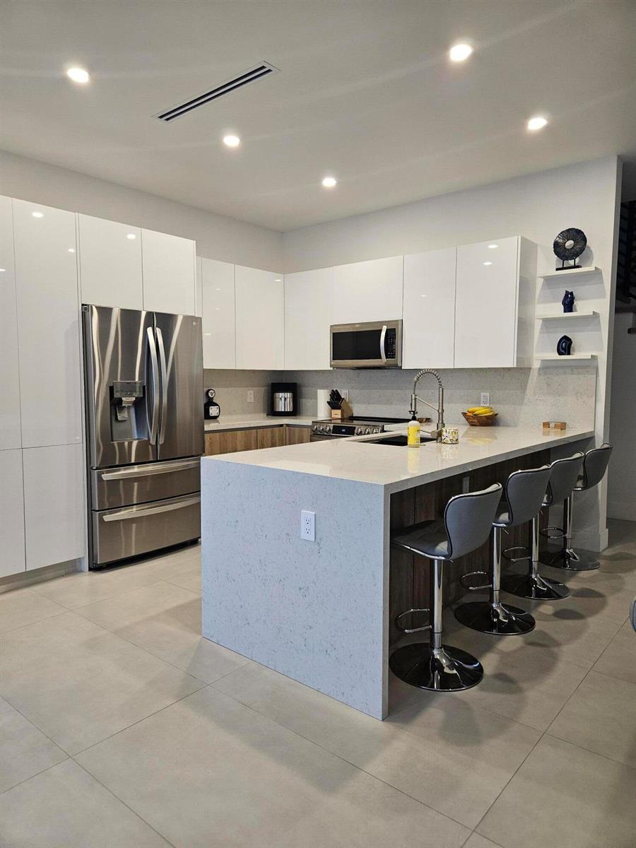 A modern kitchen features white high-gloss cabinets, a quartz waterfall island, and stainless steel appliances — 2275 SE 7th Street, Pompano Beach FL 33062, POMPANO BEACH, FL