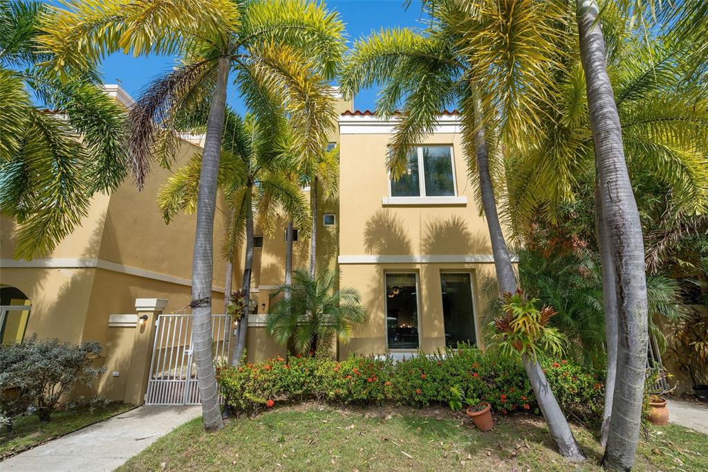 A tan two-story house exterior features palm trees, a white gate, and red flowering shrubs — 90 CANDELERO DRIVE UNIT 13, HUMACAO, PR