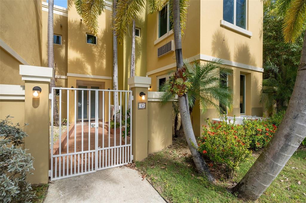 A gated entrance leads to the front door of a yellow two-story stucco home — 90 CANDELERO DRIVE UNIT 13, HUMACAO, PR