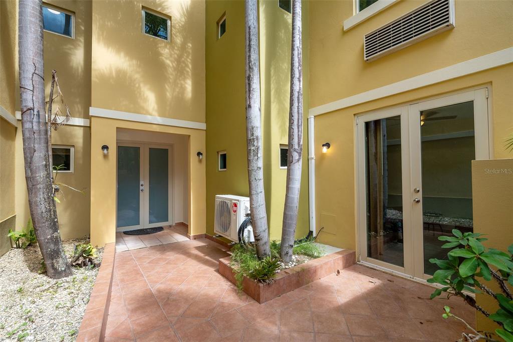 A tiled courtyard features two sets of glass doors, palm trees, and an outdoor air conditioner — 90 CANDELERO DRIVE UNIT 13, HUMACAO, PR