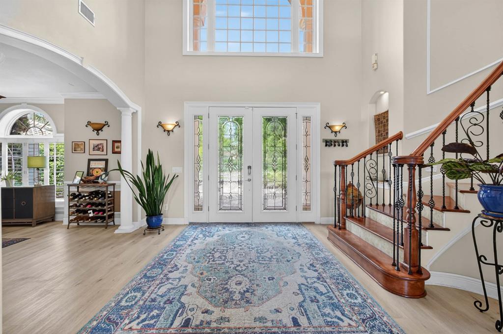 A grand foyer features a large area rug, a wooden staircase, and double glass doors — 18 HAMMOCK BEACH PARKWAY, PALM COAST, FL