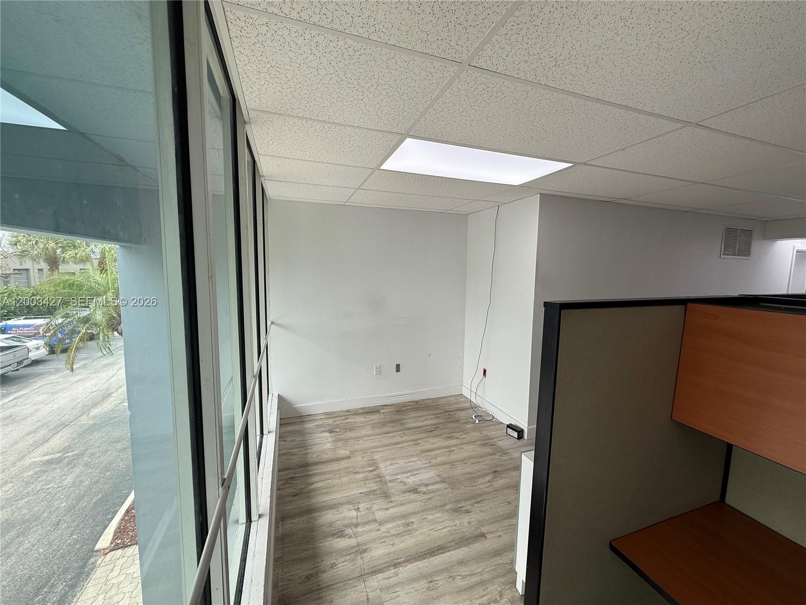An office space features wood-look flooring, a drop ceiling, and large windows overlooking a parking lot — 16155 SW 117th Ave # B18, Miami FL 33177, MIAMI, FL