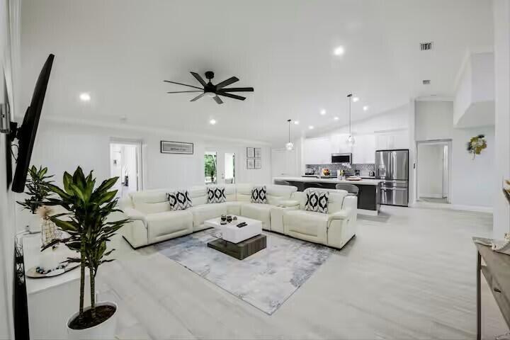 An open-concept living room with a white sectional sofa, kitchen island, and light wood flooring — 11038 Persimmon Boulevard, West Palm Beach FL 33411, WEST PALM BEACH, FL
