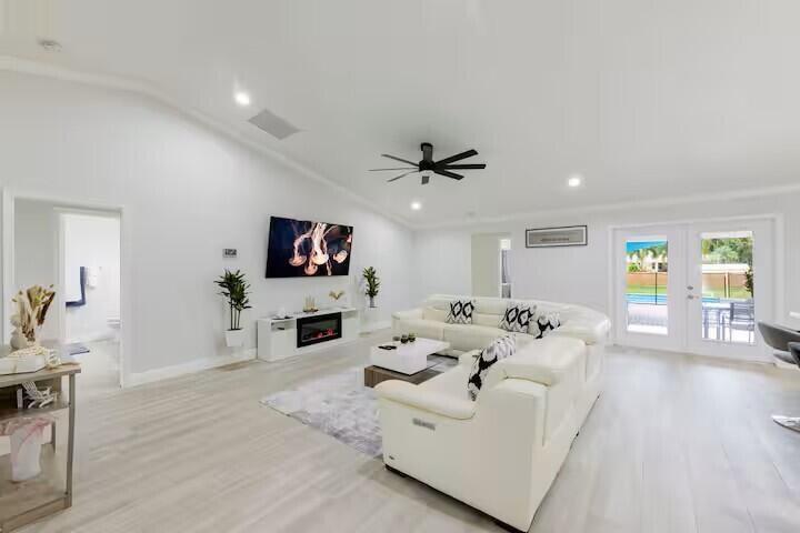 A bright living room features white walls, light wood flooring, a sectional sofa, and fireplace — 11038 Persimmon Boulevard, West Palm Beach FL 33411, WEST PALM BEACH, FL