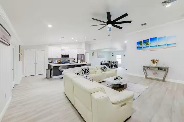 An open-concept living room and kitchen feature white cabinetry, a large sectional, and tile flooring — 11038 Persimmon Boulevard, West Palm Beach FL 33411, WEST PALM BEACH, FL