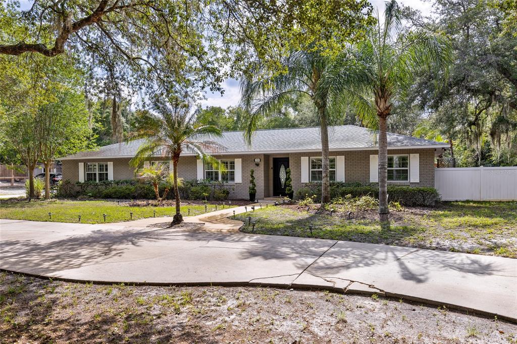 A single-story brick house with a concrete driveway, palm trees, and white window shutters — 330 HAYES ROAD, WINTER SPRINGS, FL
