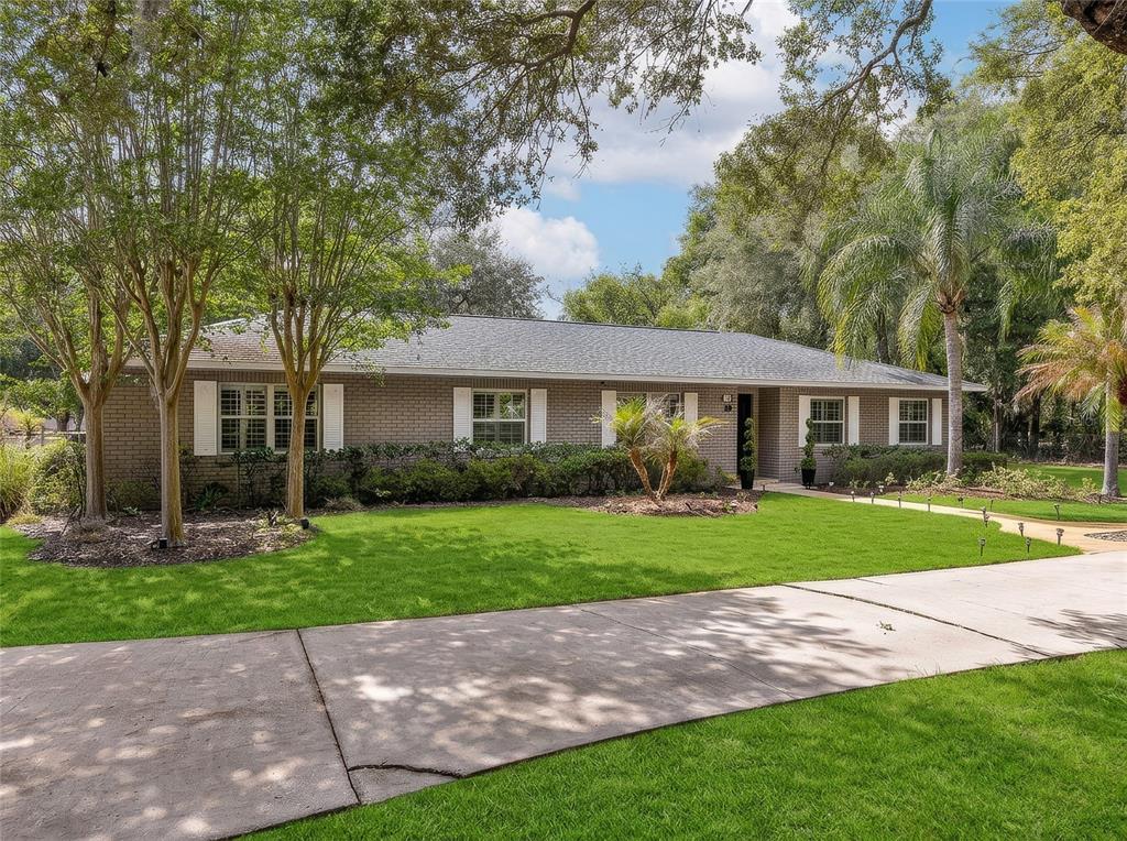 A single-story brick house with white shutters sits behind a large lawn and concrete driveway — 330 HAYES ROAD, WINTER SPRINGS, FL