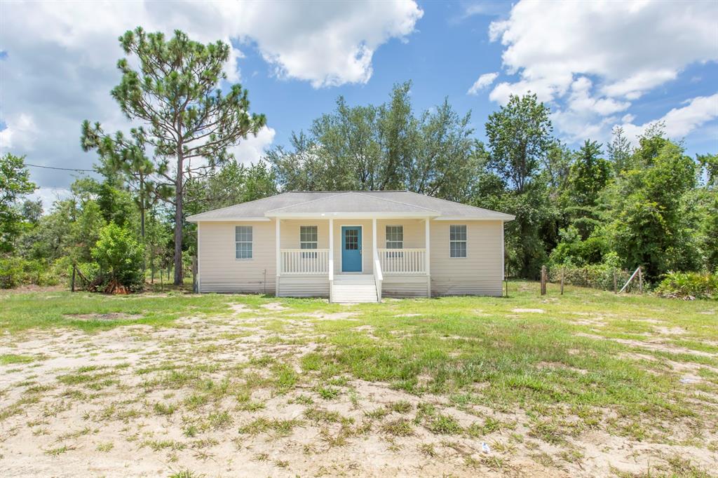 A single-story house with beige siding, a blue front door, and a covered porch — 11960 NE 67TH LANE, WILLISTON, FL