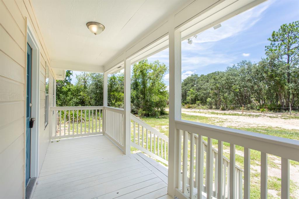 A covered wooden porch with white railings overlooks a grassy yard and a wooded area — 11960 NE 67TH LANE, WILLISTON, FL