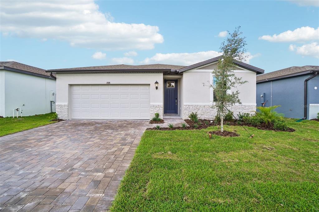 A single-story house with a white stucco facade, stone accents, and a paved driveway — 13696 UMBER FOREST STREET, HUDSON, FL