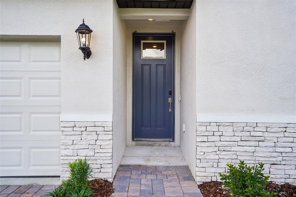 A blue front door with a small window is set between white stone-accented walls — 13696 UMBER FOREST STREET, HUDSON, FL