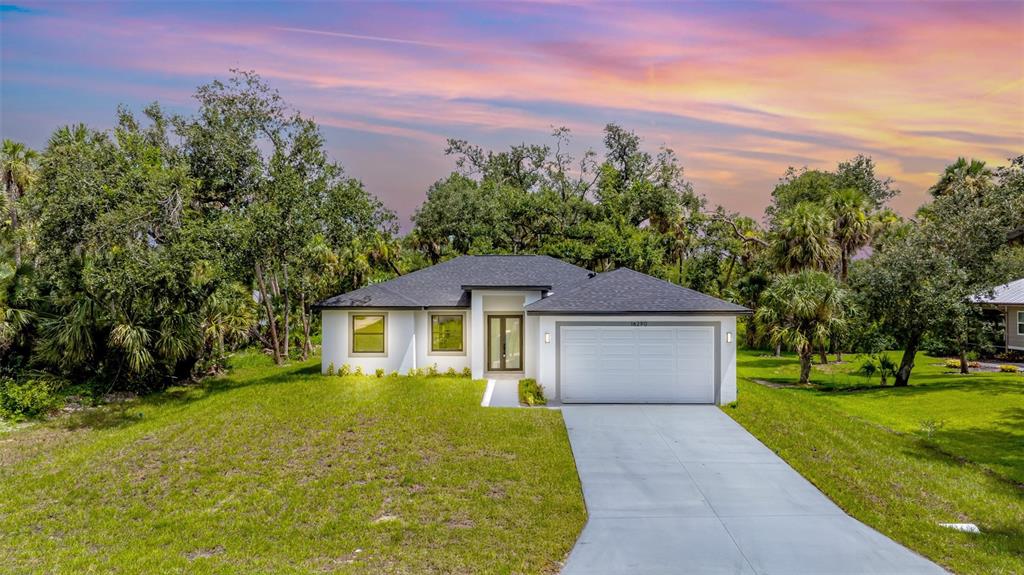 A single-story white house with a dark roof and a two-car garage sits on grass — 16290 BANYAN AVENUE, PORT CHARLOTTE, FL
