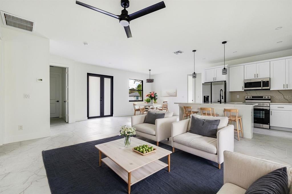 An open-concept living room and kitchen featuring white cabinetry, marble-look tile floors, and a ceiling fan — 16290 BANYAN AVENUE, PORT CHARLOTTE, FL