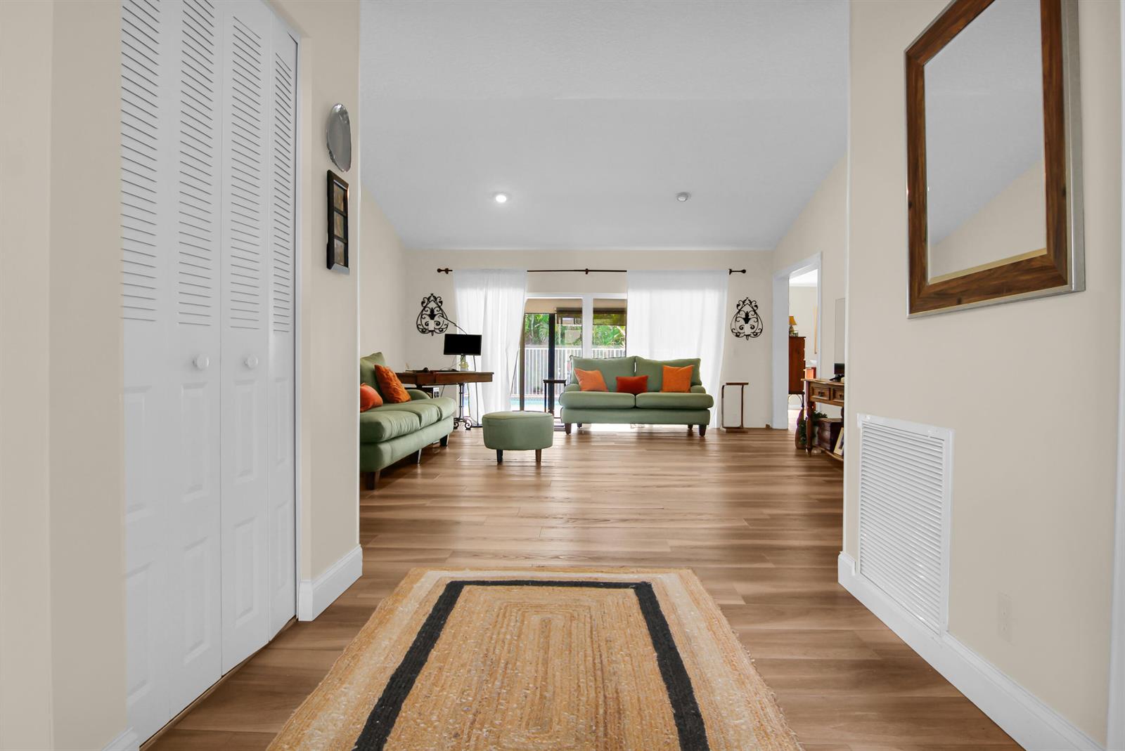 A hallway with wood-look flooring leads into a living room featuring two green sofas — 18375 104th Terrace S, Boca Raton FL 33498, BOCA RATON, FL