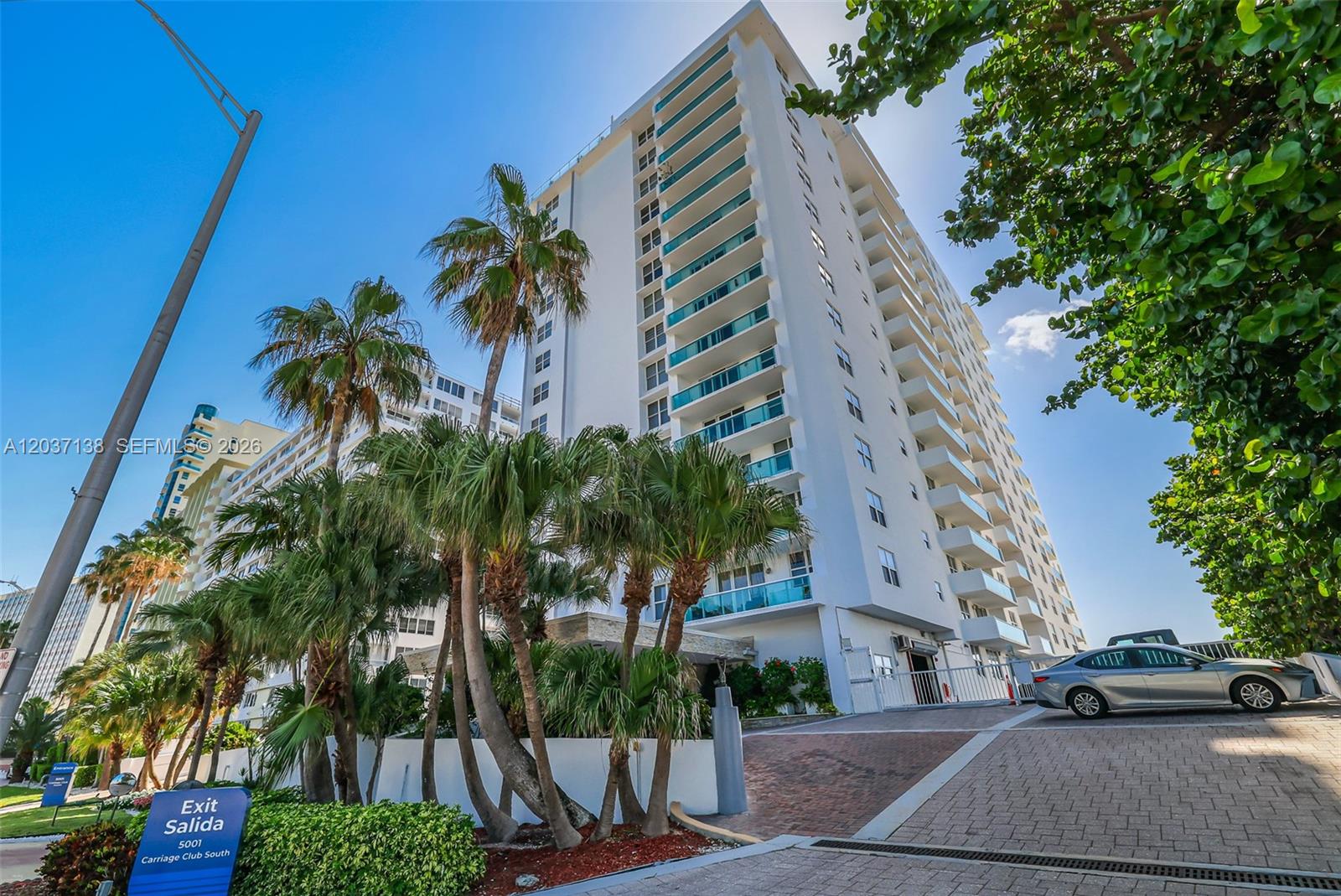 A tall white residential building stands behind palm trees and a paved driveway — 5001 Collins Ave # 6E, Miami Beach FL 33140, MIAMI BEACH, FL
