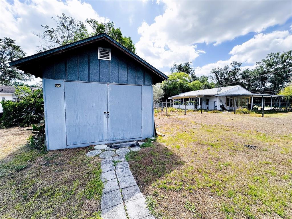 A blue wooden storage shed stands in a grassy yard near a single-story house — 1690 S MCADOO AVENUE, BARTOW, FL