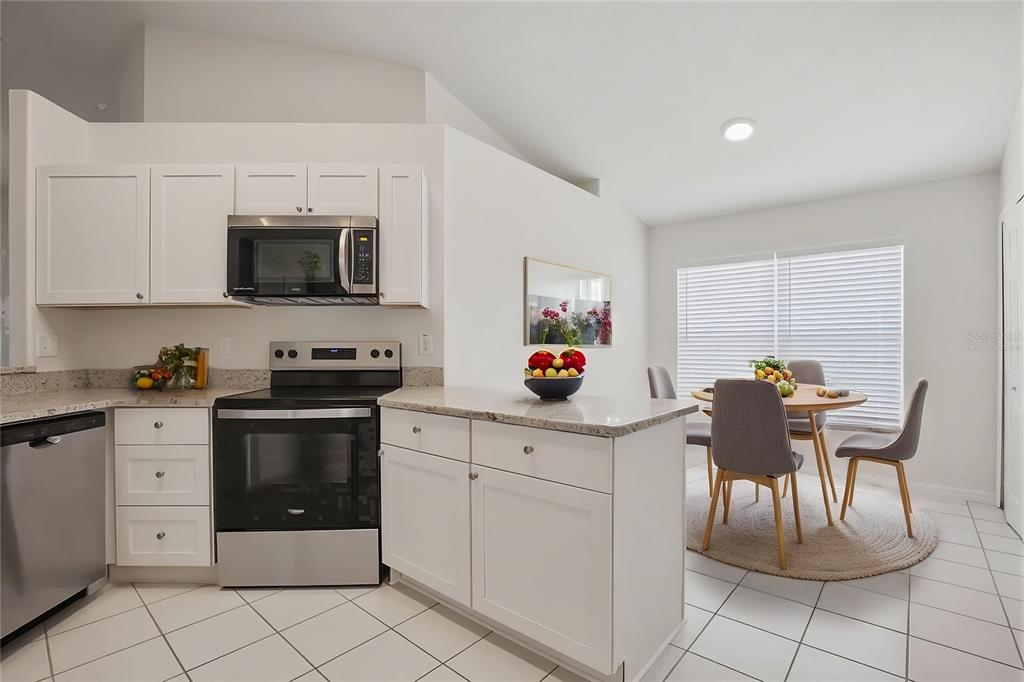 A kitchen with white cabinets, stainless steel appliances, and a dining area with a round table — 1353 CRIMSON CLOVER LANE, WESLEY CHAPEL, FL