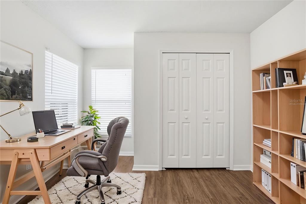 A home office features a wooden desk, a gray chair, a bookshelf, and white closets — 1353 CRIMSON CLOVER LANE, WESLEY CHAPEL, FL