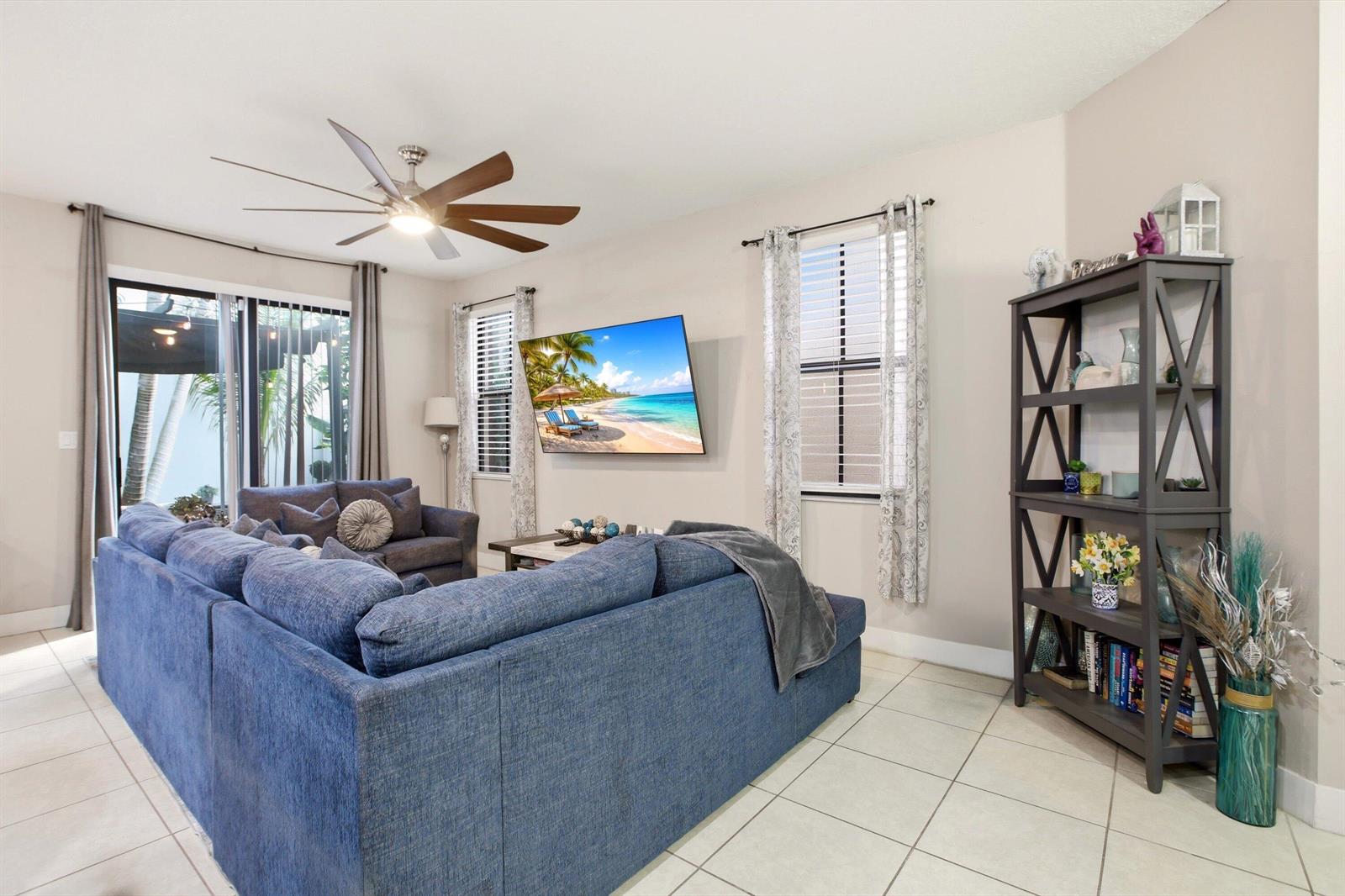 A living room features a blue sectional sofa, a wall-mounted television, and a tall bookshelf — 6026 Pine Tree Way # 6026, Riviera Beach FL 33410, RIVIERA BEACH, FL