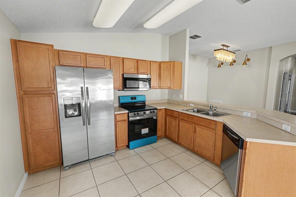 A kitchen with light wood cabinets, stainless steel appliances, and beige tile flooring — 4693 HARTS BROOK LANE, MULBERRY, FL