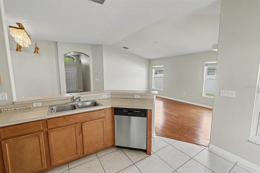 A kitchen with wood cabinets and a stainless steel dishwasher overlooks an adjacent living area — 4693 HARTS BROOK LANE, MULBERRY, FL