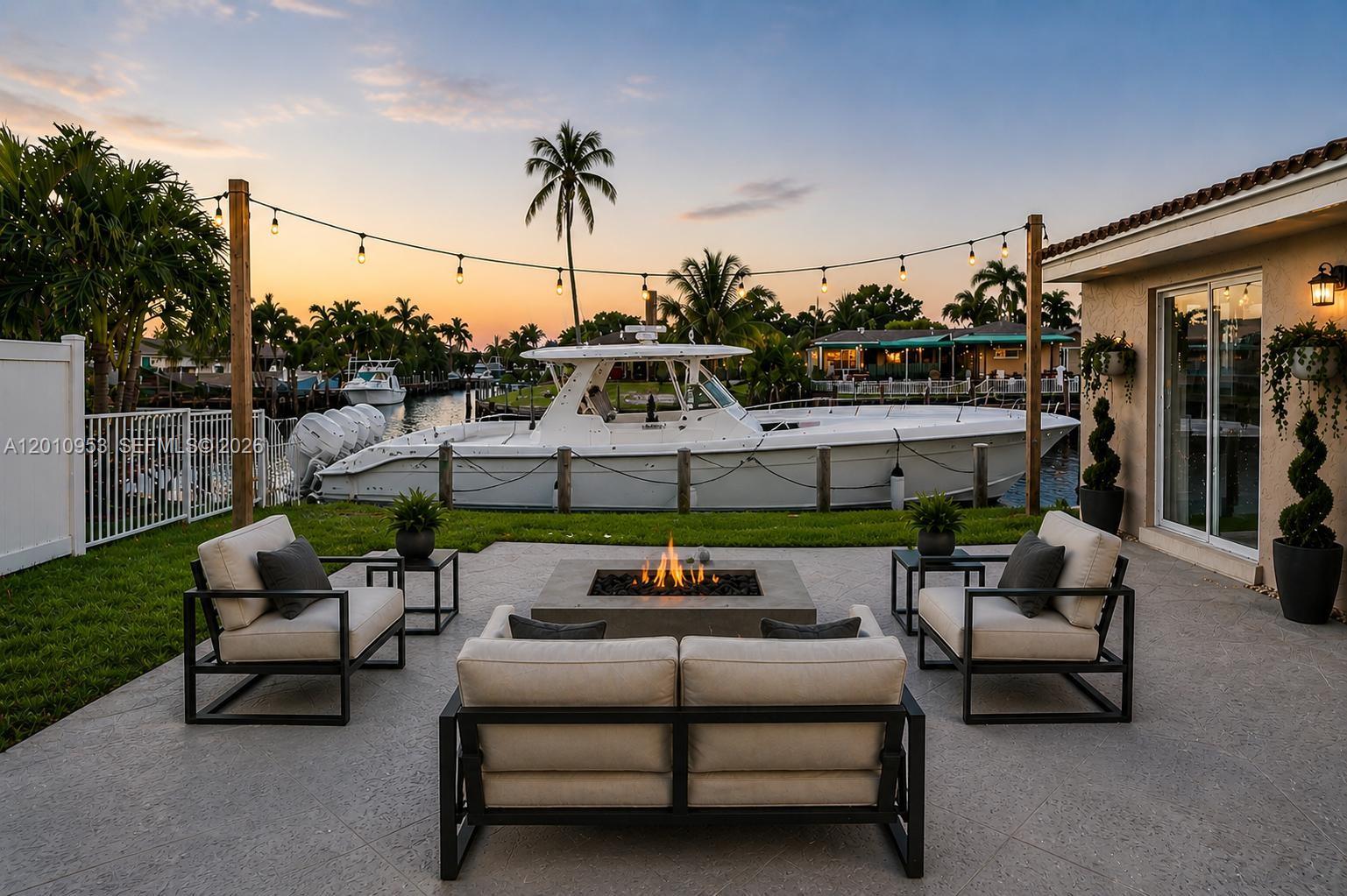 A patio with a fire pit and seating overlooks a canal with a docked boat — 949 SE 10th Ct, Pompano Beach FL 33060, POMPANO BEACH, FL