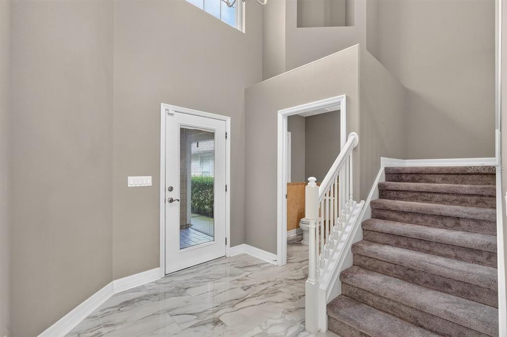 An entryway features marble-look tile flooring, a white front door, and carpeted stairs — 1975 RUTGERS PLACE, PORT ORANGE, FL
