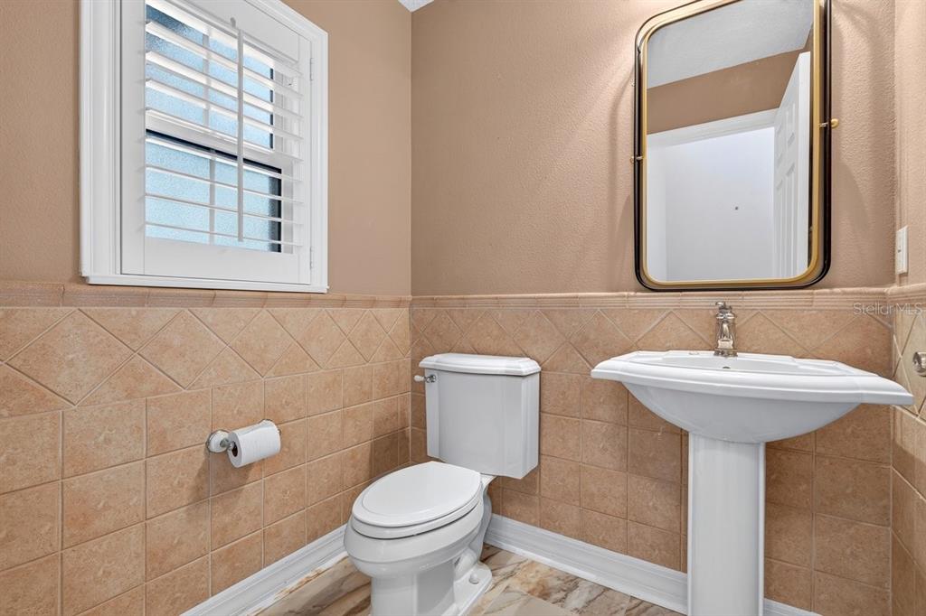 A powder room features tan tile wainscoting, a pedestal sink, a toilet, and a framed mirror — 1975 RUTGERS PLACE, PORT ORANGE, FL