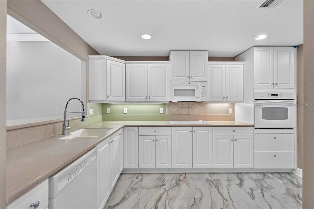 A kitchen features white cabinets, a beige countertop, a built-in oven, and marble-patterned tile flooring — 1975 RUTGERS PLACE, PORT ORANGE, FL