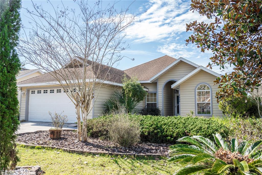 A single-story house with tan siding, a two-car garage, and a landscaped front yard — 11774 NW 60TH DRIVE, ALACHUA, FL