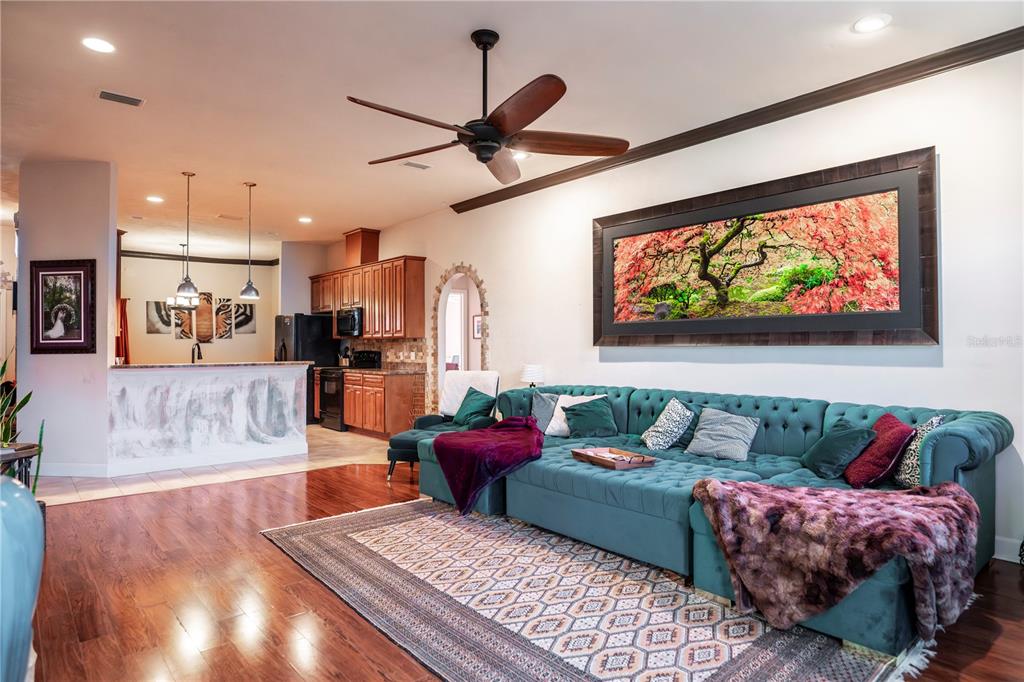 A living room with a teal tufted sectional sofa opens to a kitchen with wood cabinets — 11774 NW 60TH DRIVE, ALACHUA, FL