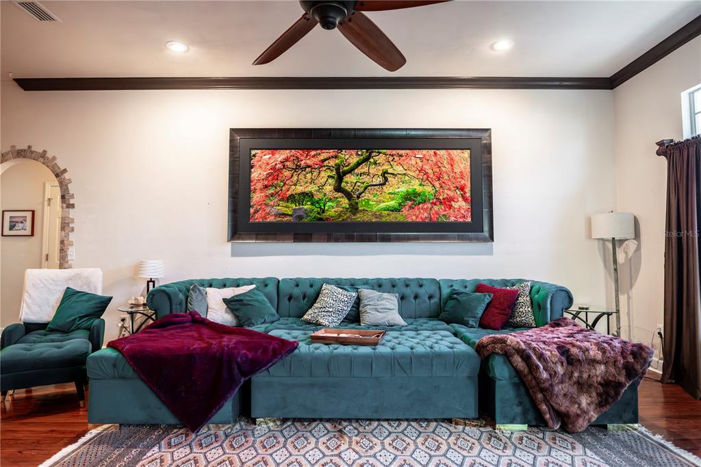 A living room features a large teal tufted sectional sofa beneath a wide landscape painting — 11774 NW 60TH DRIVE, ALACHUA, FL