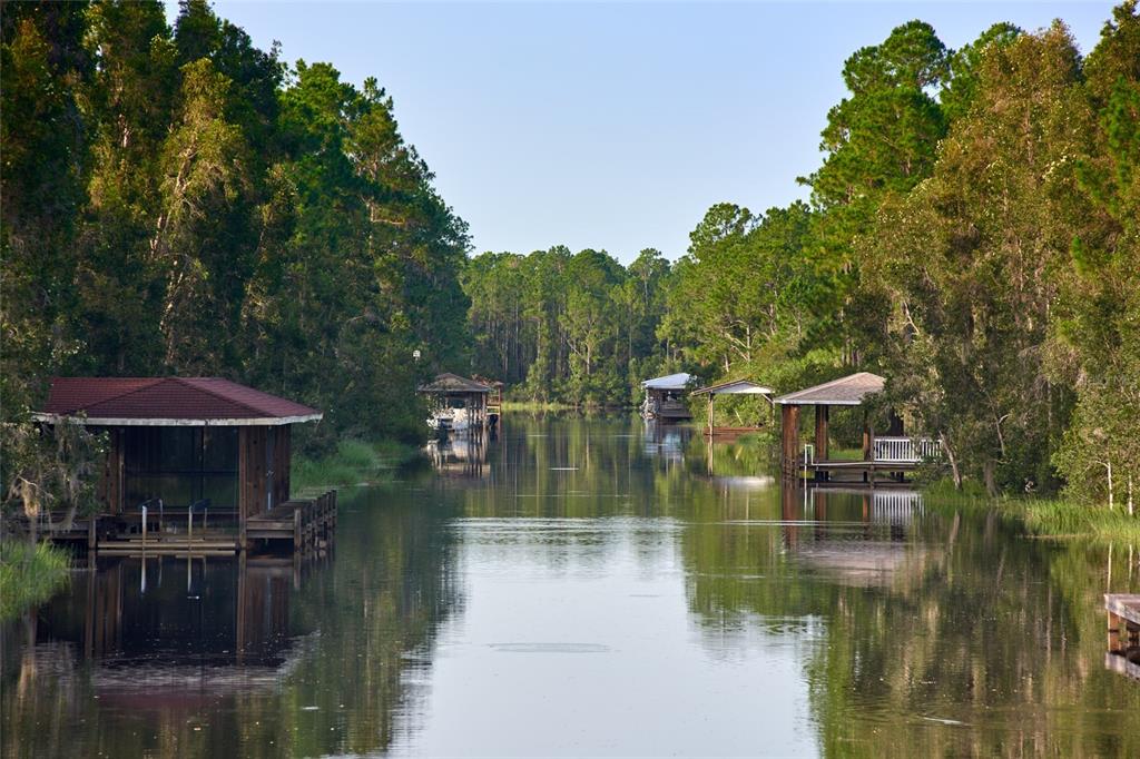 A canal lined with trees features several wooden boat docks and covered slips — 824 BOUGAINVILLE DRIVE, INDIAN LAKE ESTATES, FL