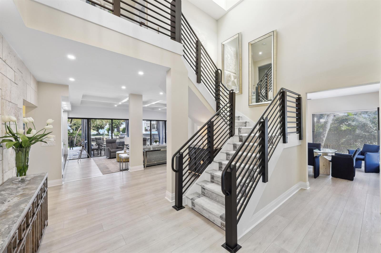 A bright foyer features light wood floors, a central staircase with black railings, and mirrors — 125 Marlin Drive, Ocean Ridge FL 33435, OCEAN RIDGE, FL