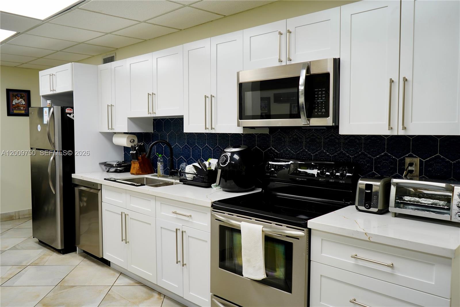 A kitchen features white cabinets, stainless steel appliances, and a dark blue hexagonal tile backsplash — 150 Westward Dr # 2, Miami Springs FL 33166, MIAMI SPRINGS, FL