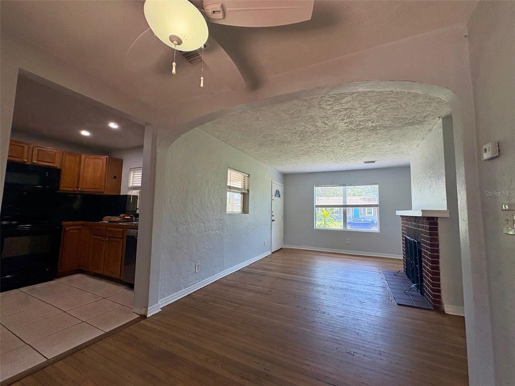 A living room with wood flooring and a brick fireplace opens into a tiled kitchen — 3455 7TH AVENUE N, ST PETERSBURG, FL