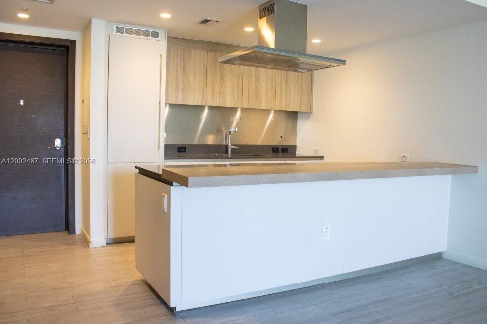 A modern kitchen features light wood cabinets, a stainless steel range hood, and a peninsula — 1000 Brickell Plz # 1906, Miami FL 33131, MIAMI, FL