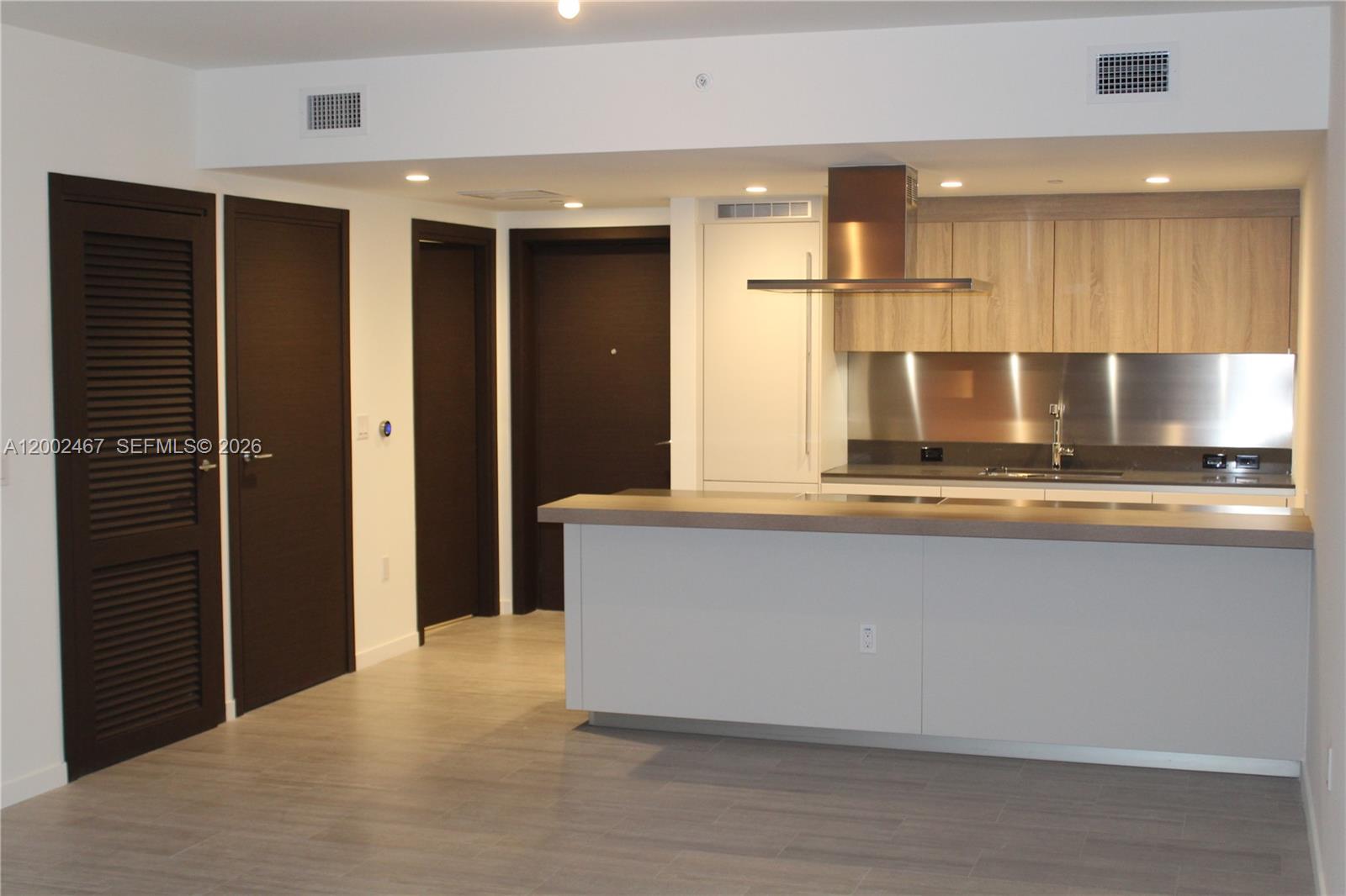 A modern kitchen features light wood cabinets, a stainless steel backsplash, and a gray island — 1000 Brickell Plz # 1906, Miami FL 33131, MIAMI, FL