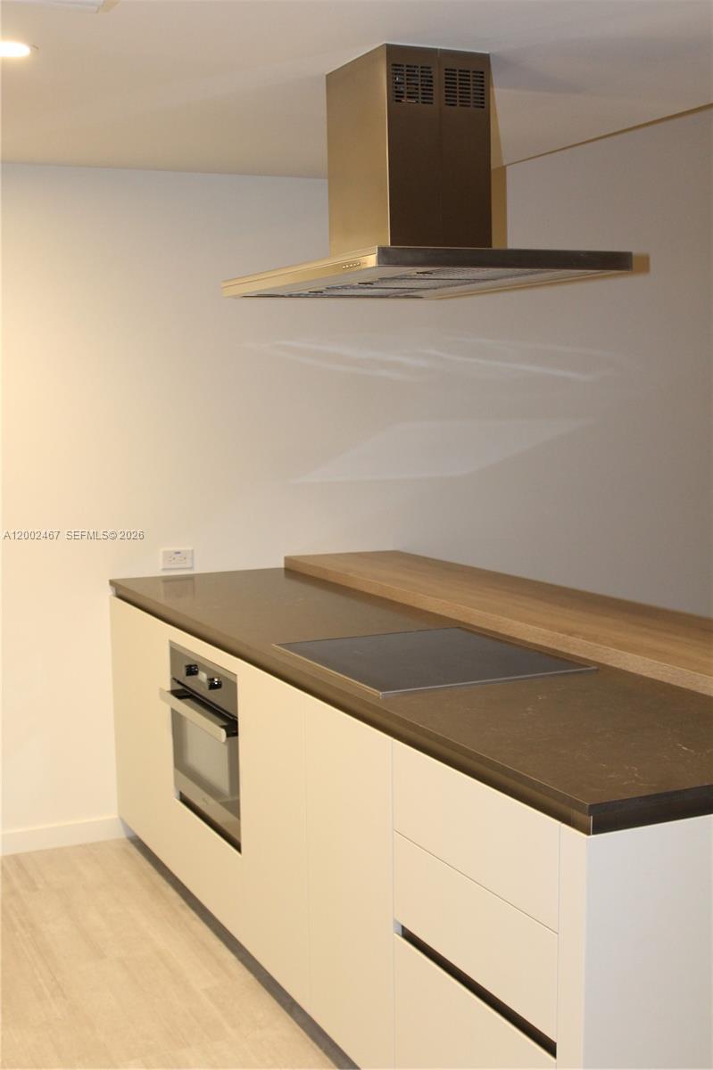 A modern kitchen features white cabinets, a dark countertop, a built-in oven, and a range hood — 1000 Brickell Plz # 1906, Miami FL 33131, MIAMI, FL
