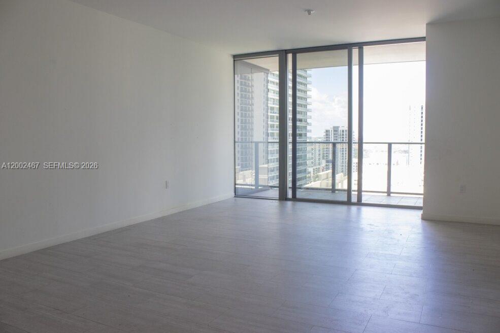 An empty room features light-colored wood-look flooring, white walls, and a large glass balcony door — 1000 Brickell Plz # 1906, Miami FL 33131, MIAMI, FL