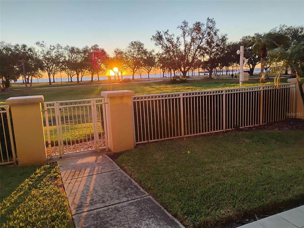 A metal gate and fence enclose a grassy yard overlooking a sunset at the beach — 555 5TH AVENUE NE UNIT 183, ST PETERSBURG, FL