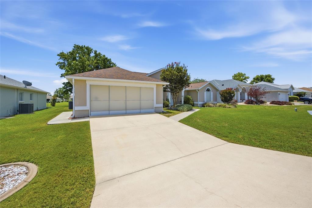 A beige house with a two-car garage and a concrete driveway sits on a lawn — 5450 NW 25TH LOOP, OCALA, FL
