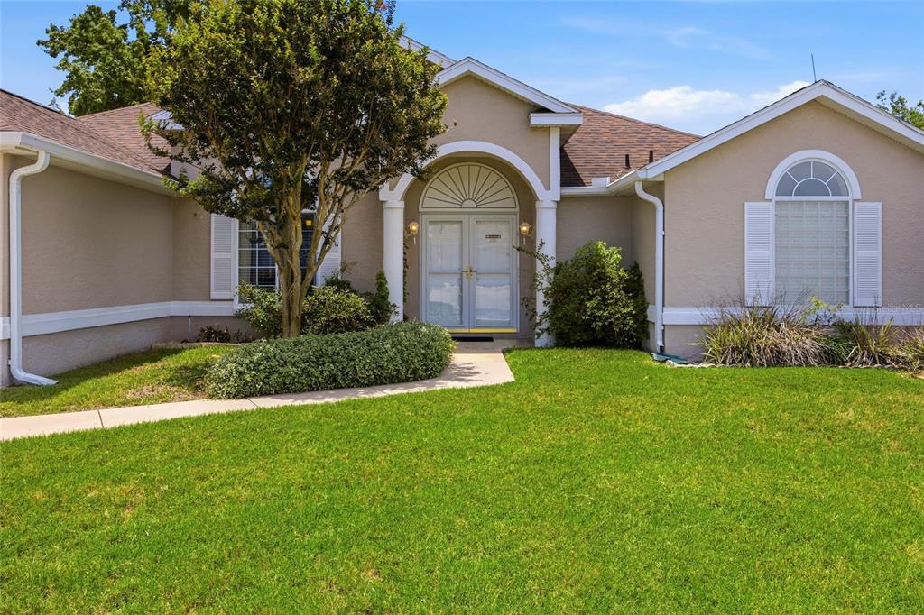A single-story house with a beige stucco exterior, double front doors, and a grassy lawn — 5450 NW 25TH LOOP, OCALA, FL