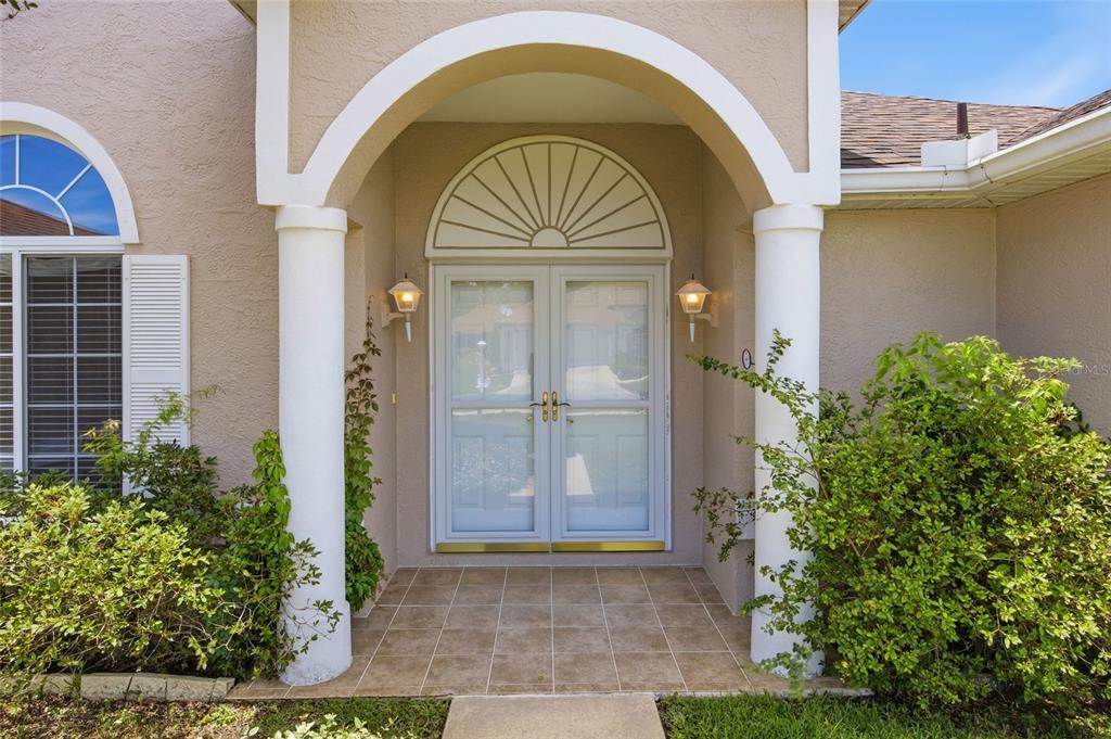 A covered entryway features double glass doors, a decorative arched transom, and two white columns — 5450 NW 25TH LOOP, OCALA, FL