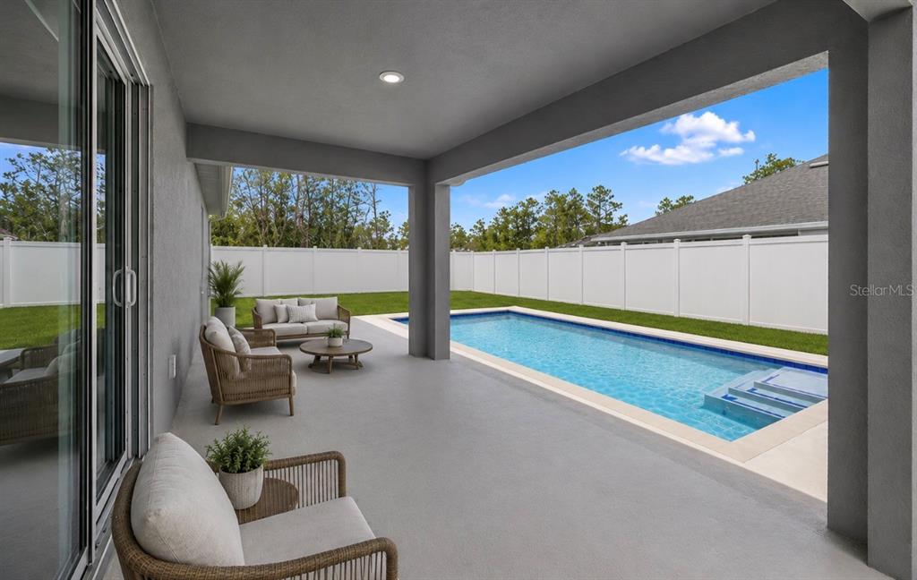 A covered patio features outdoor furniture overlooking a rectangular swimming pool and a fenced yard — 18 FLAMINGO DRIVE, PALM COAST, FL