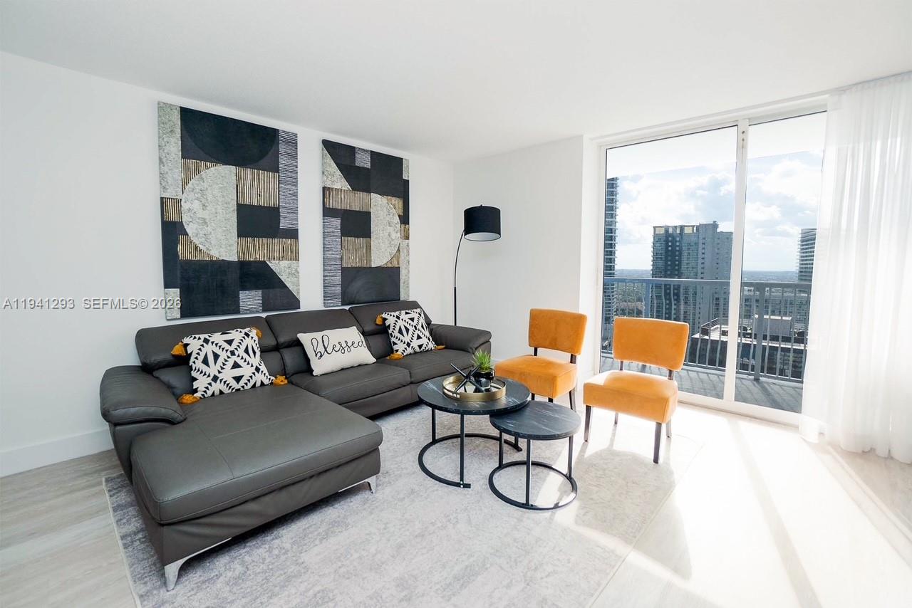 A living room features a grey sectional sofa, two orange chairs, and floor-to-ceiling windows — 1200 Brickell Bay Dr # 3524, Miami FL 33131, MIAMI, FL