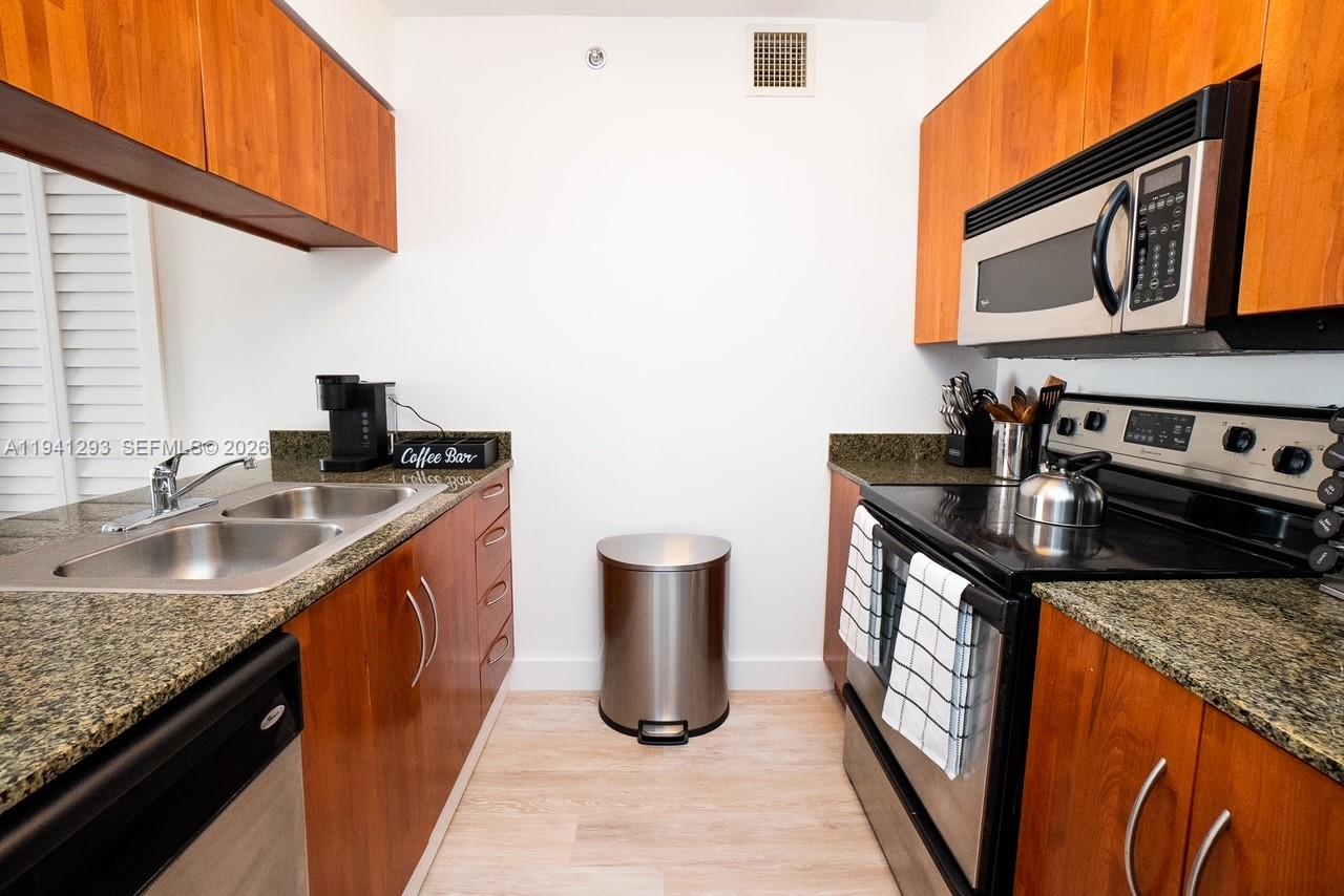 A galley kitchen features wood cabinets, granite countertops, stainless steel appliances, and light wood flooring — 1200 Brickell Bay Dr # 3524, Miami FL 33131, MIAMI, FL