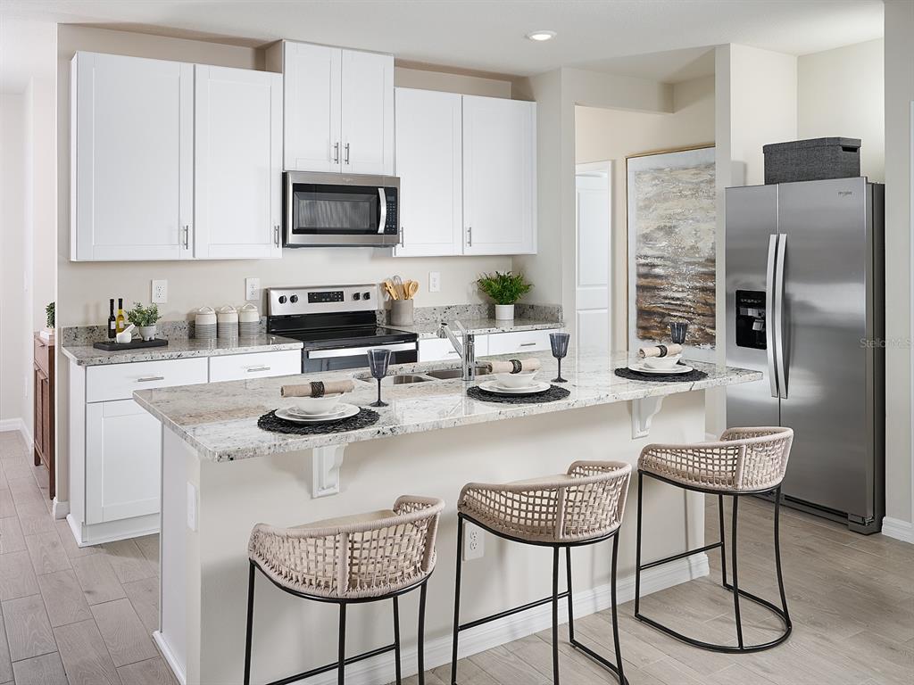 A kitchen features white cabinets, granite countertops, stainless steel appliances, and three woven bar stools — 4305 RIVER BEACON BOULEVARD, DAVENPORT, FL