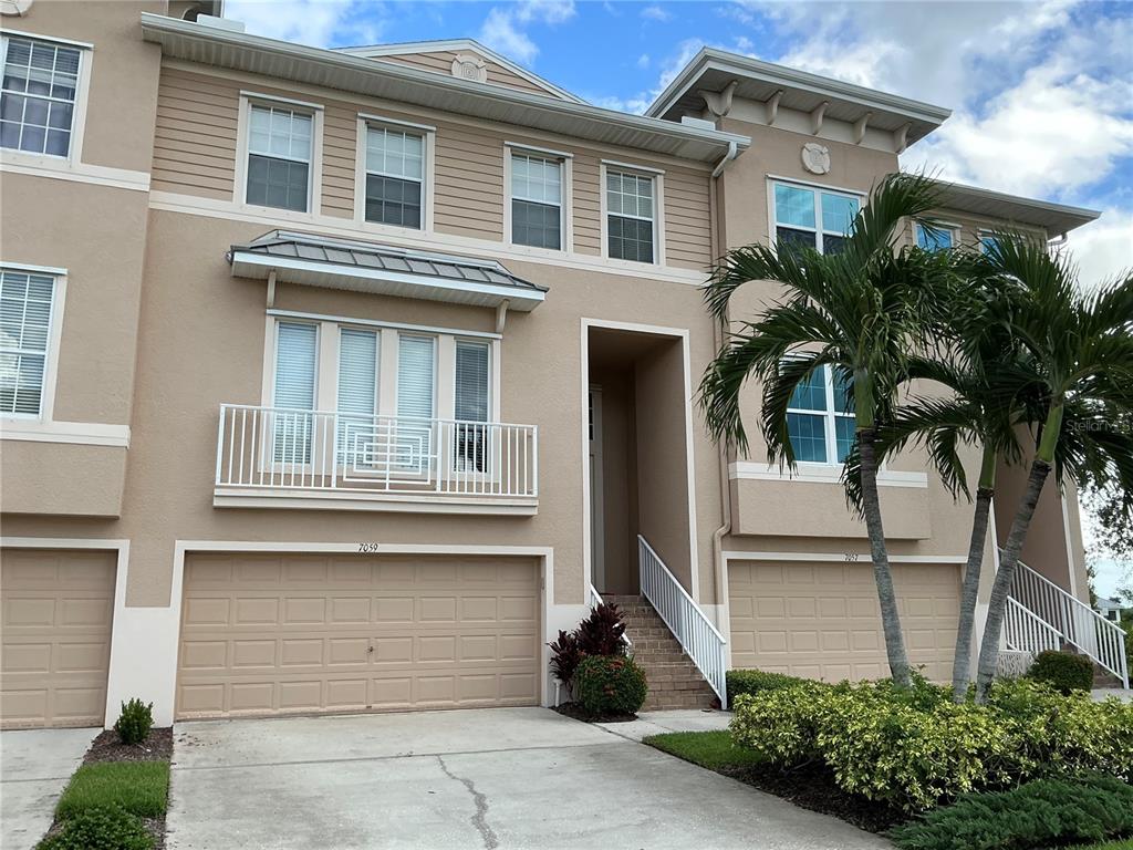 A multi-story townhouse exterior features tan siding, beige stucco, a balcony, and two garage doors — 7059 ISLAMORADA CIRCLE, SEMINOLE, FL